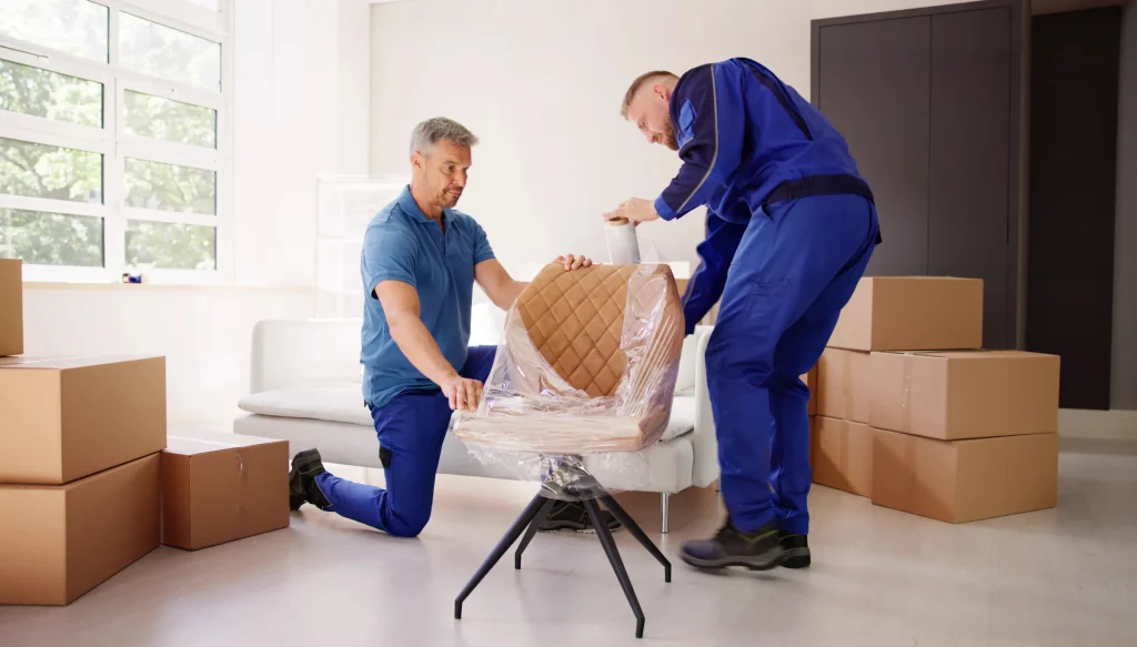 Two movers wrapping an upholstered chair in protective stretch film