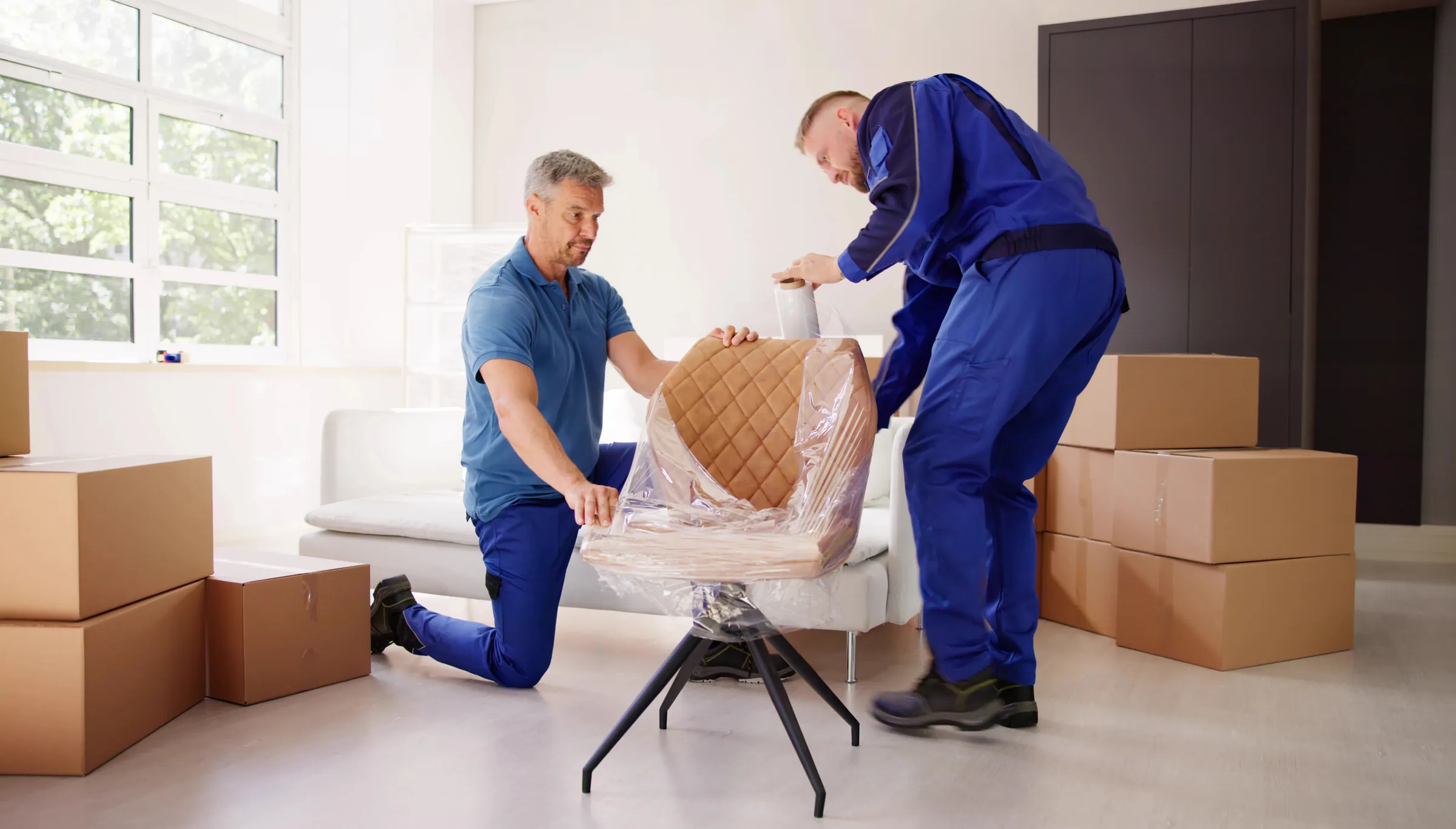 Two movers wrapping an upholstered chair in protective stretch film
