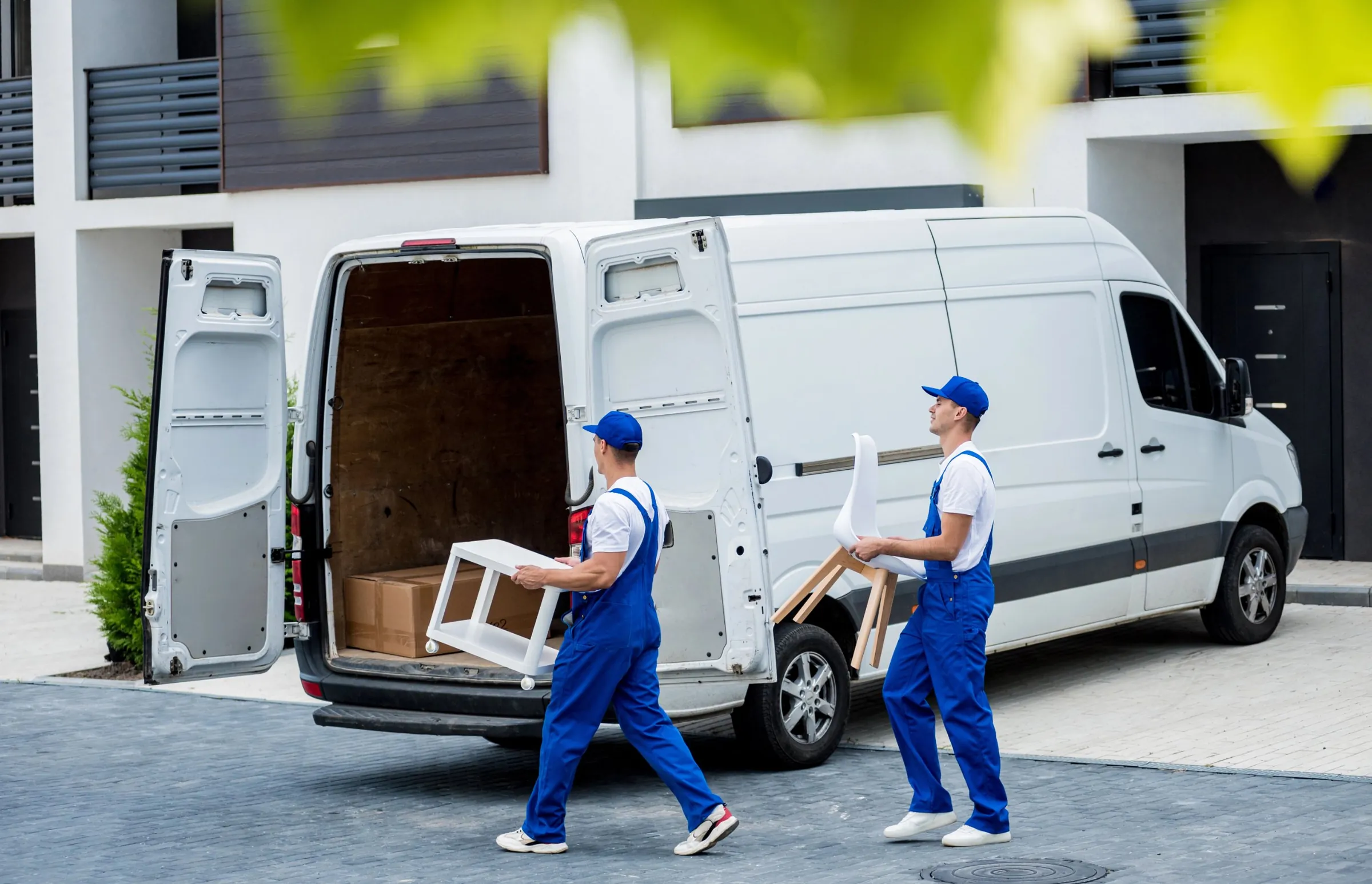 Two movers carrying furniture to a van outside a residential building