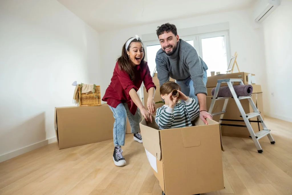 Family laughing as they push their son around in a moving box in their new home